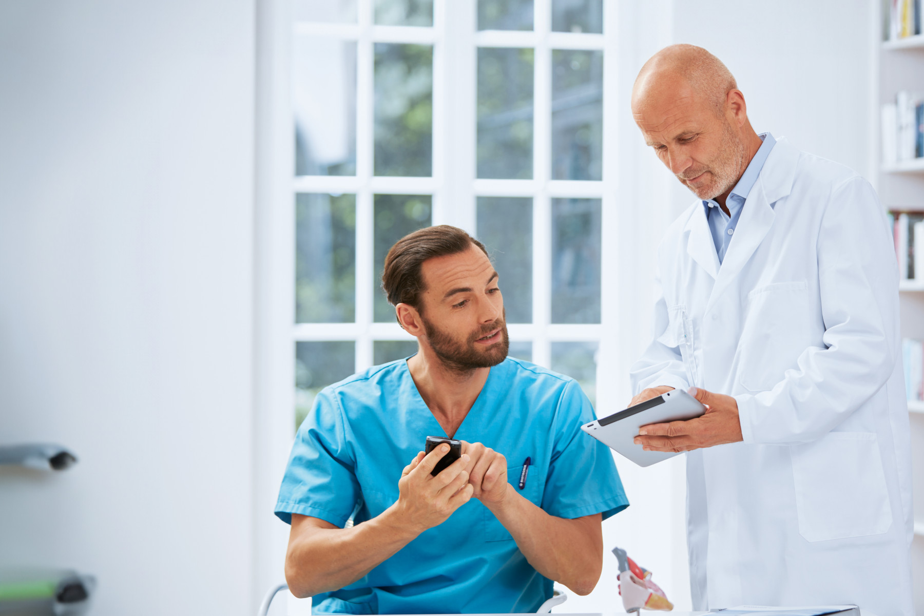 Ein Arzt zeigt einem medizinischen Fachangestellten (MFA) die Messwerte eines Patienten und schlägt vor, den Patienten telefonisch zu kontaktieren.