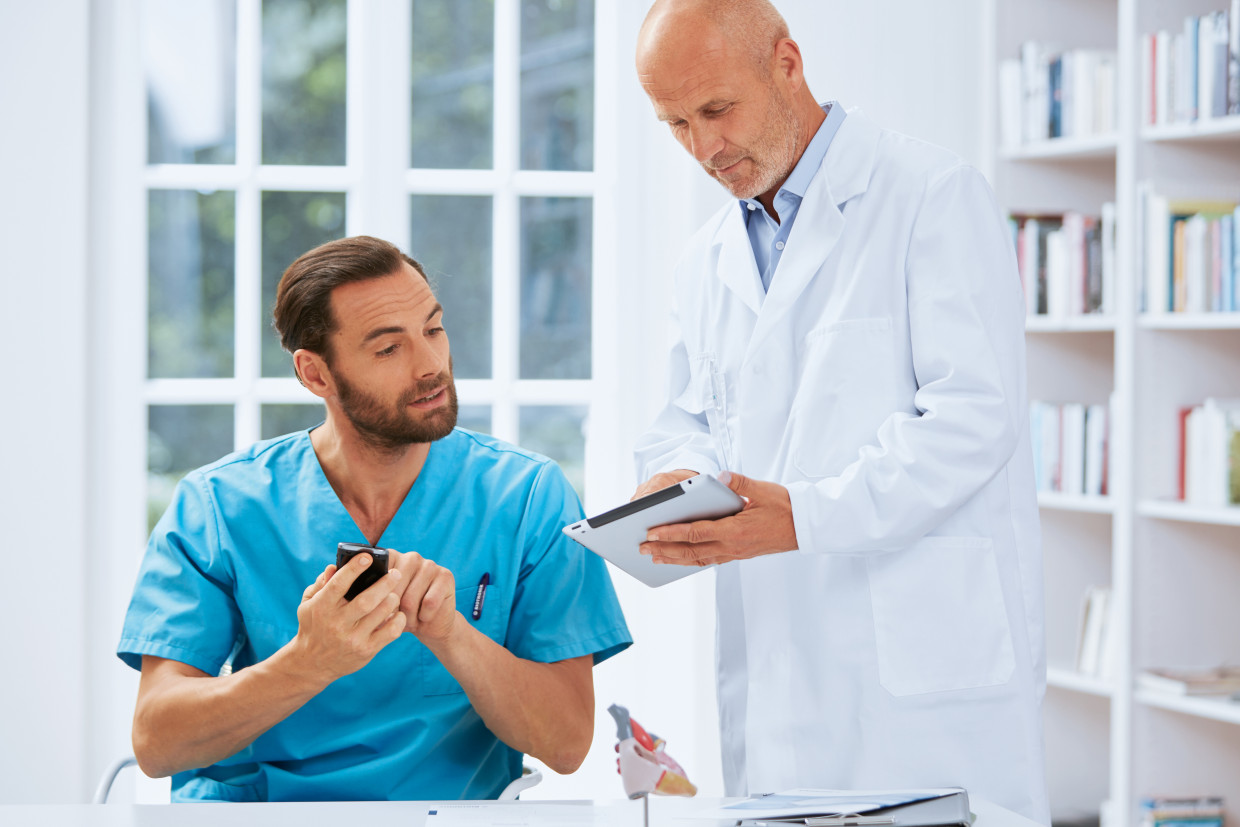 Ein Arzt zeigt einem medizinischen Fachangestellten (MFA) die Messwerte eines Patienten und schlägt vor, den Patienten telefonisch zu kontaktieren.