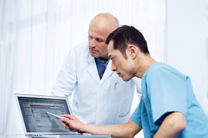 Ein Arzt und ein Telemonitoring-Fachangestellte analysieren die Alarme von Patienten mit Herzinsuffizienz auf einem Laptop