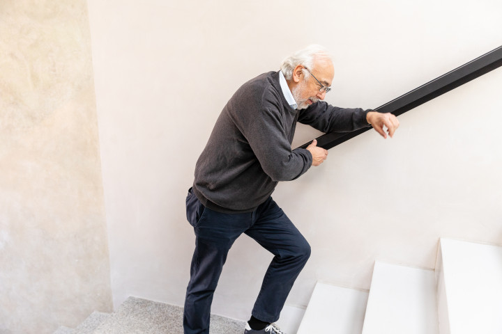 Ein Patient mit Herzinsuffizienz steigt eine Treppe hinauf und wirkt dabei sehr erschöpft.
